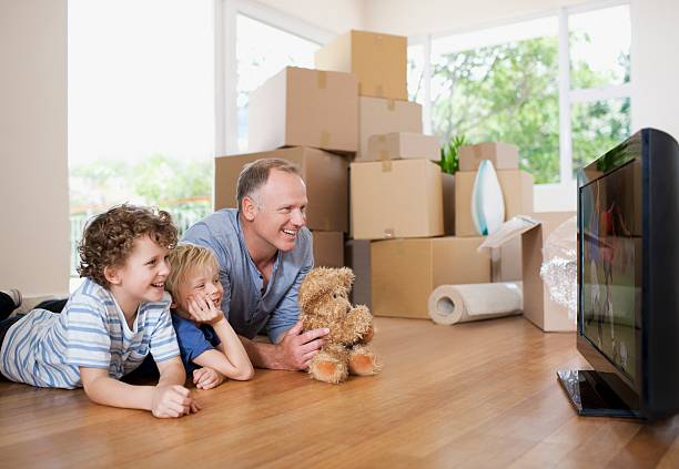 Father and Two Kids Laying on the Floor in Front of the TV With Packed Boxes Ready for iMOVE NYC Crew