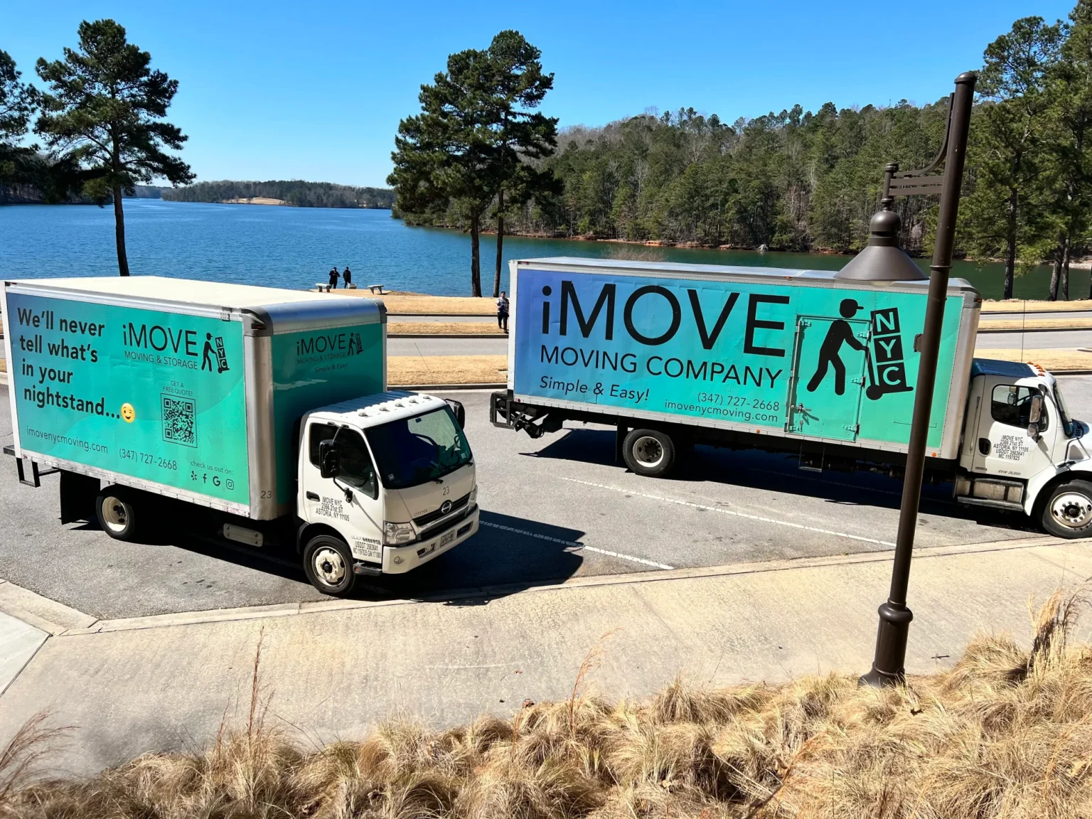 Two Turquoise iMOVE NYC Trucks Parked in Front of Beautiful Lake on a Sunny Day